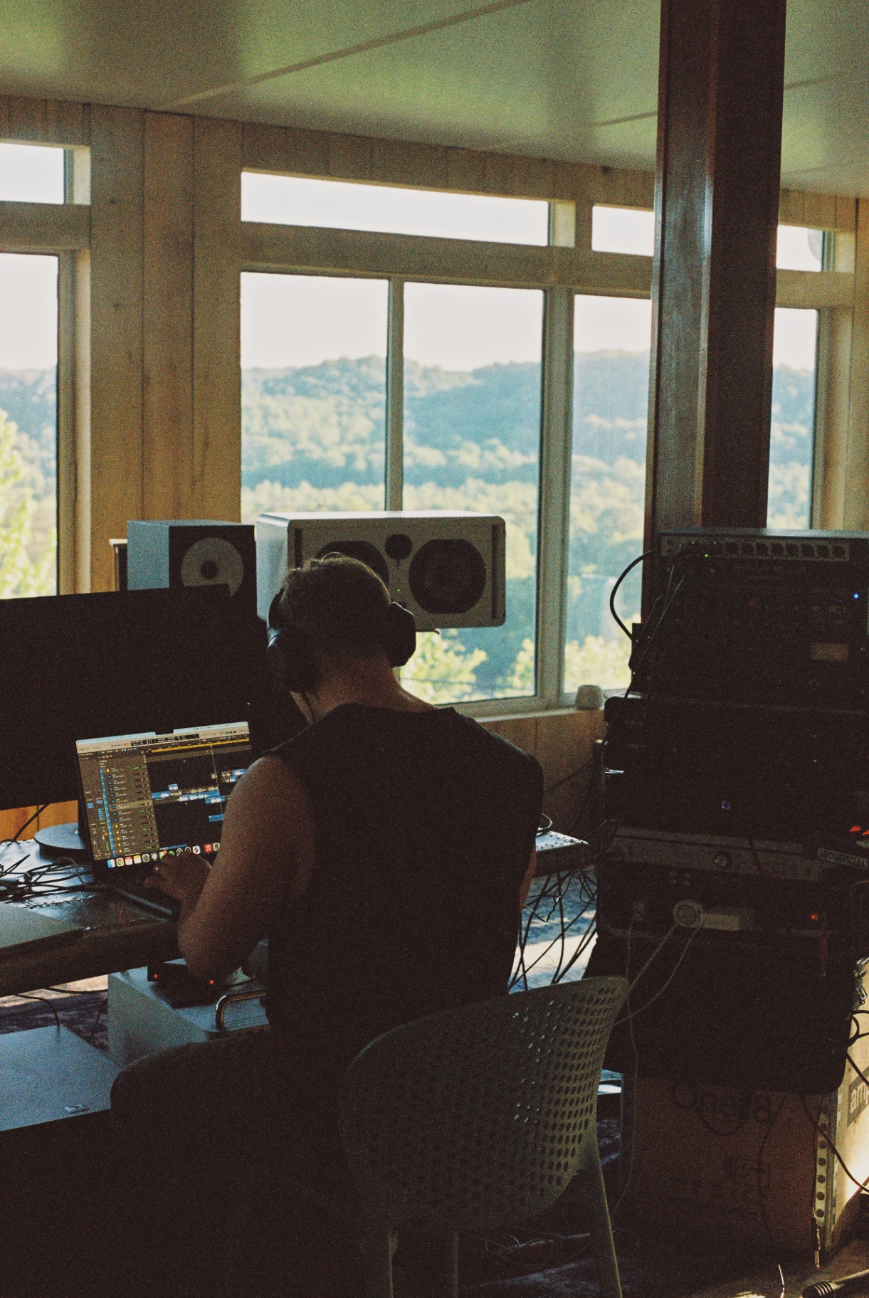 Engineer at the desk, headphones on, session open on the screen, hills through the window