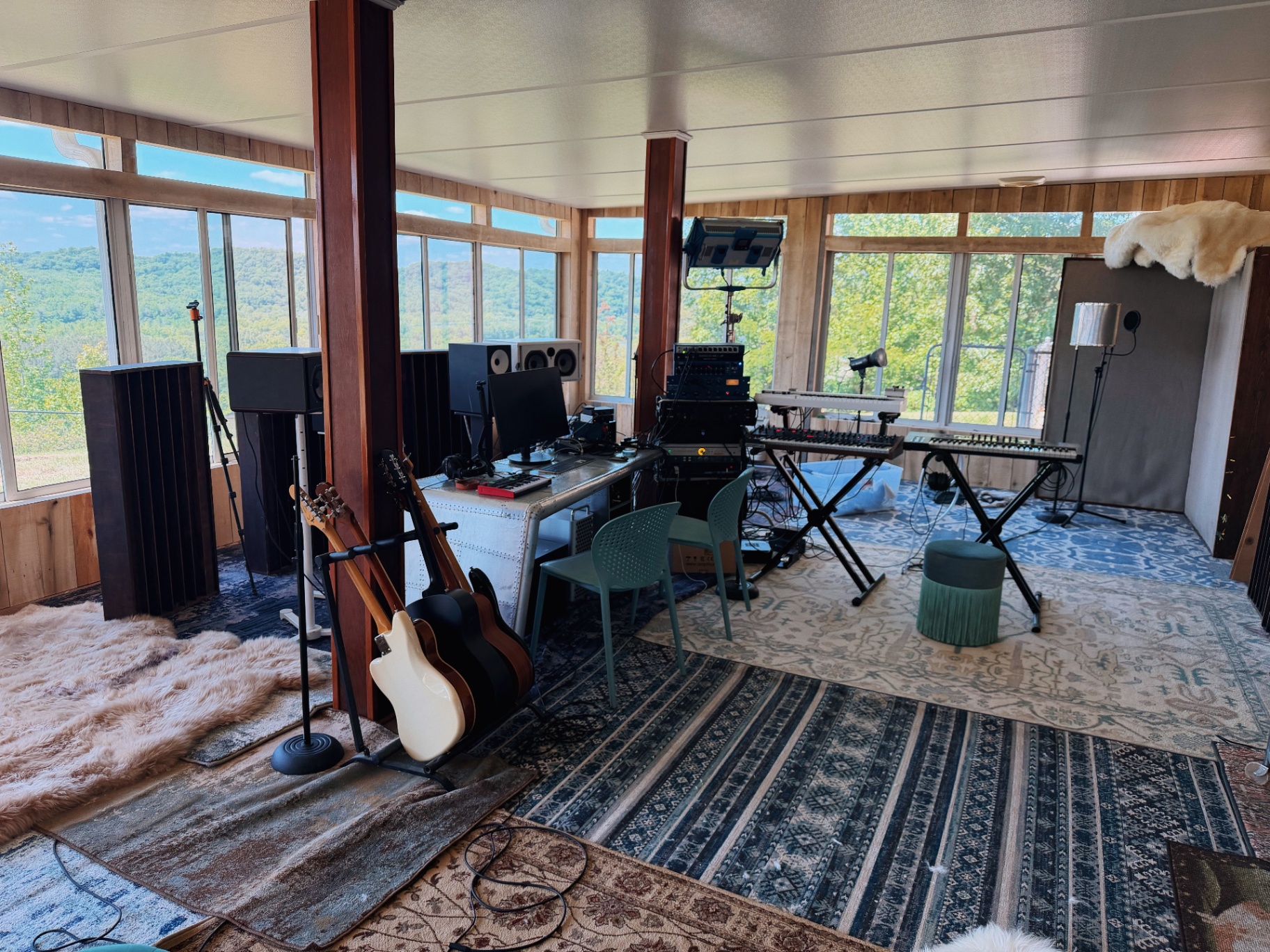 Recording studio with keyboards, guitars, and monitors under a wall of windows